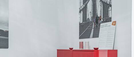 A room with a white table and red chairs, a red cabinet, and a poster of a bridge.