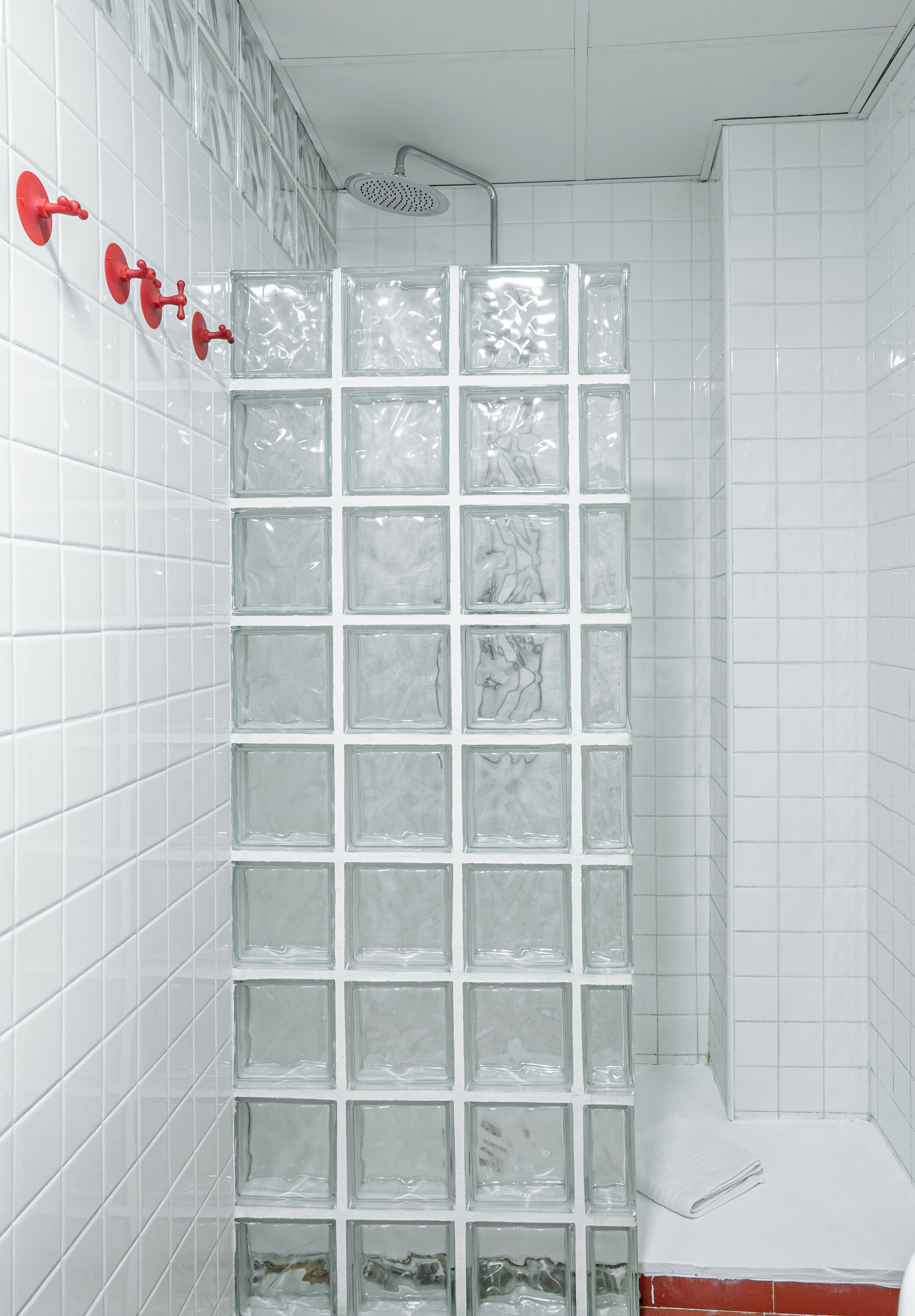 Ein Badezimmer mit weiß gefliesten Wänden, einer Duschkabine aus Glas und einem roten Duschkopf.