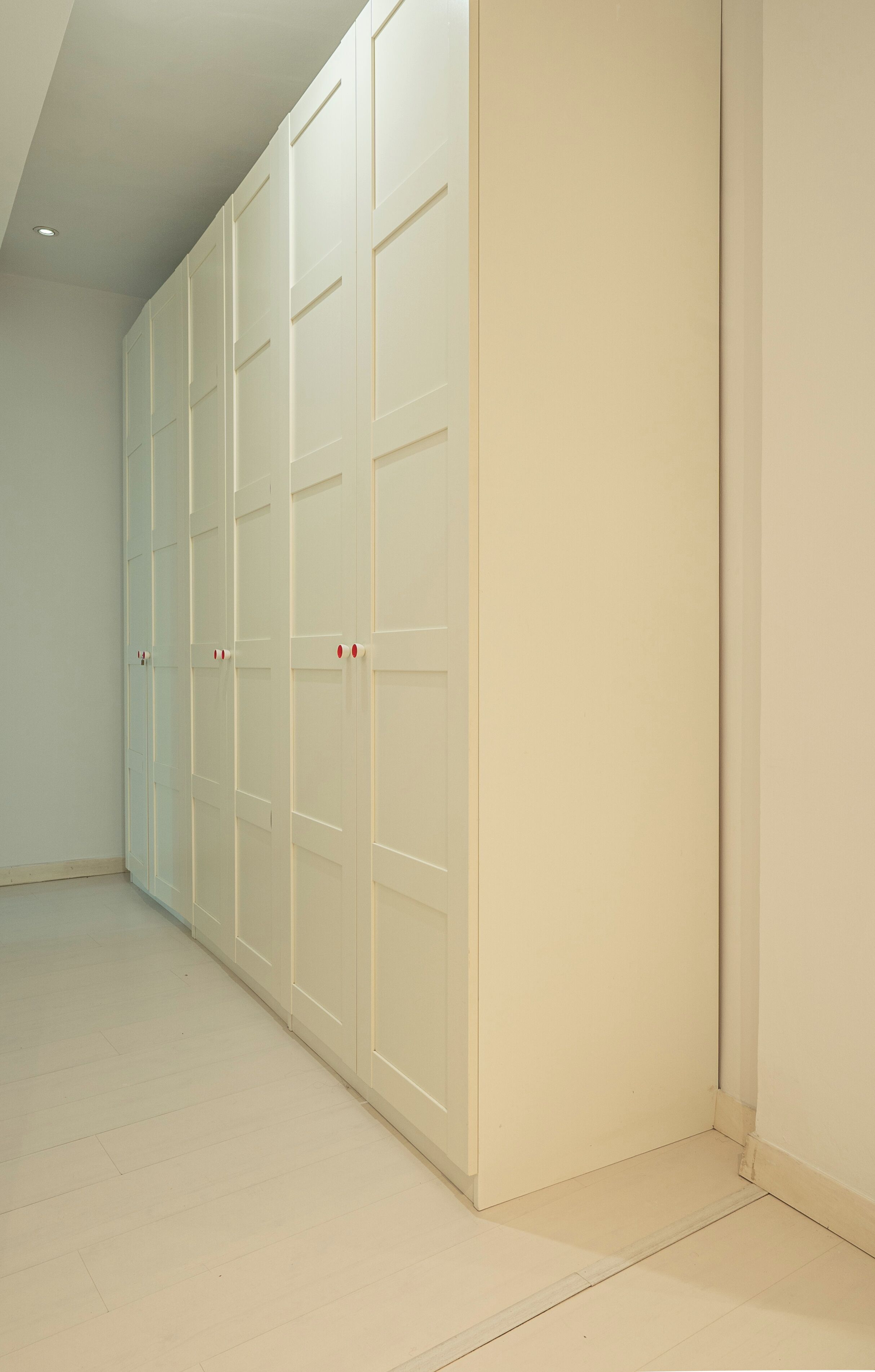 Ein großer, weißer begehbarer Kleiderschrank mit mehreren Türen und Fliesenboden.