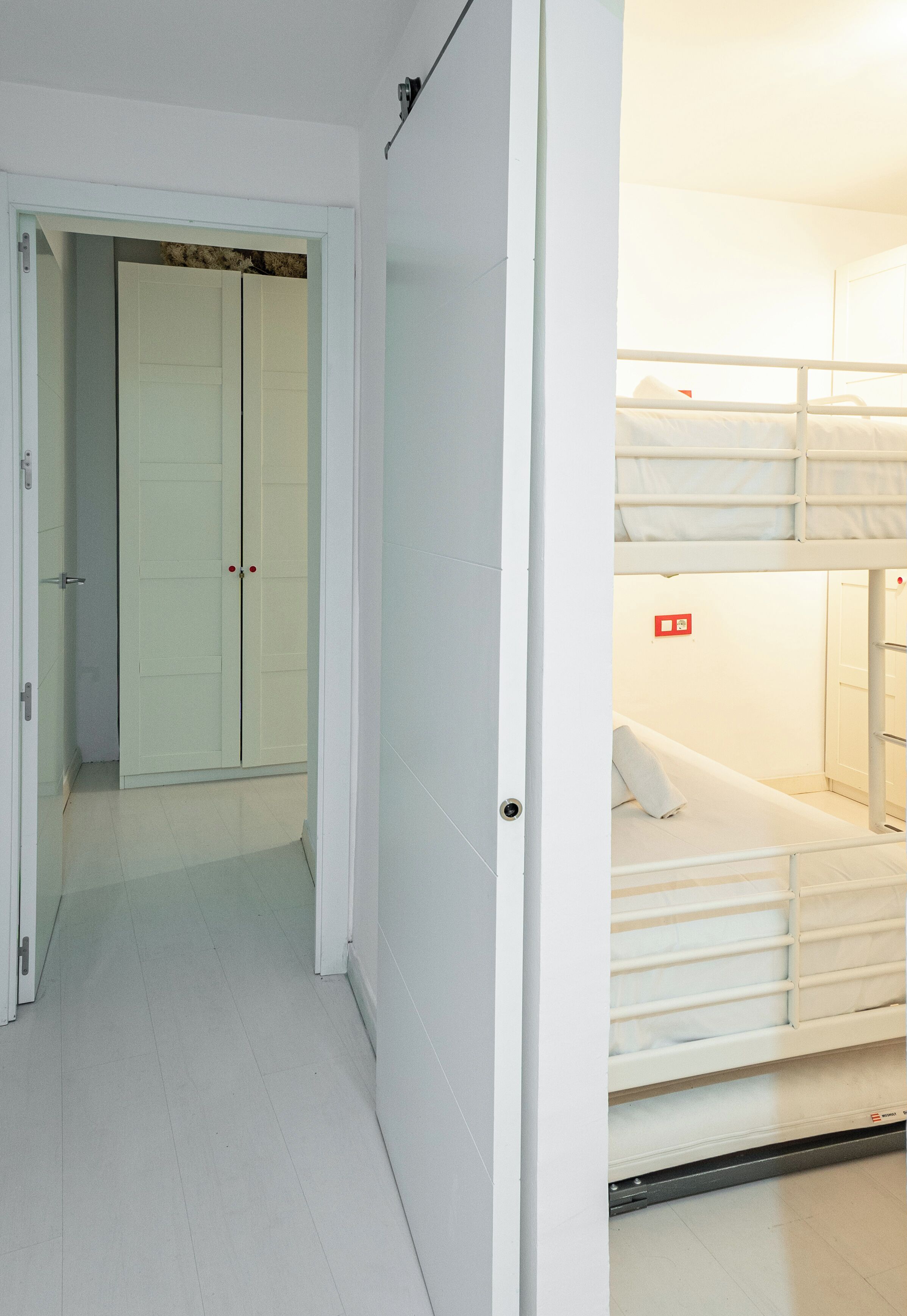 A room with a bunk bed, a wardrobe, and a door leading to another room.