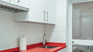Une cuisine moderne avec des meubles blancs, un plan de travail rouge, un four encastré et une porte vitrée donnant sur un coin repas.