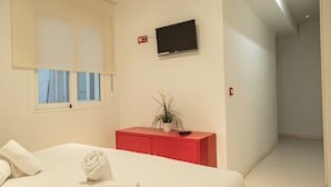 Une chambre d’hôtel avec un lit, un téléviseur fixé au mur, une armoire rouge et une fenêtre avec des rideaux.