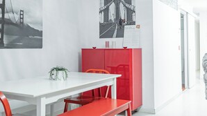 Une pièce moderne avec une table blanche, des bancs rouges et un meuble rouge. Deux photographies en noir et blanc sont accrochées aux murs.