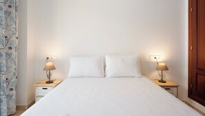 A neatly made bed with white linens, two bedside tables with lamps, and a wooden wardrobe. - Stay U-nique Apartment Alderete (Málaga)