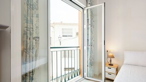 A bedroom with a balcony, a bed, a nightstand with a lamp, and a window with curtains. - Stay U-nique Apartment Alderete (Málaga)