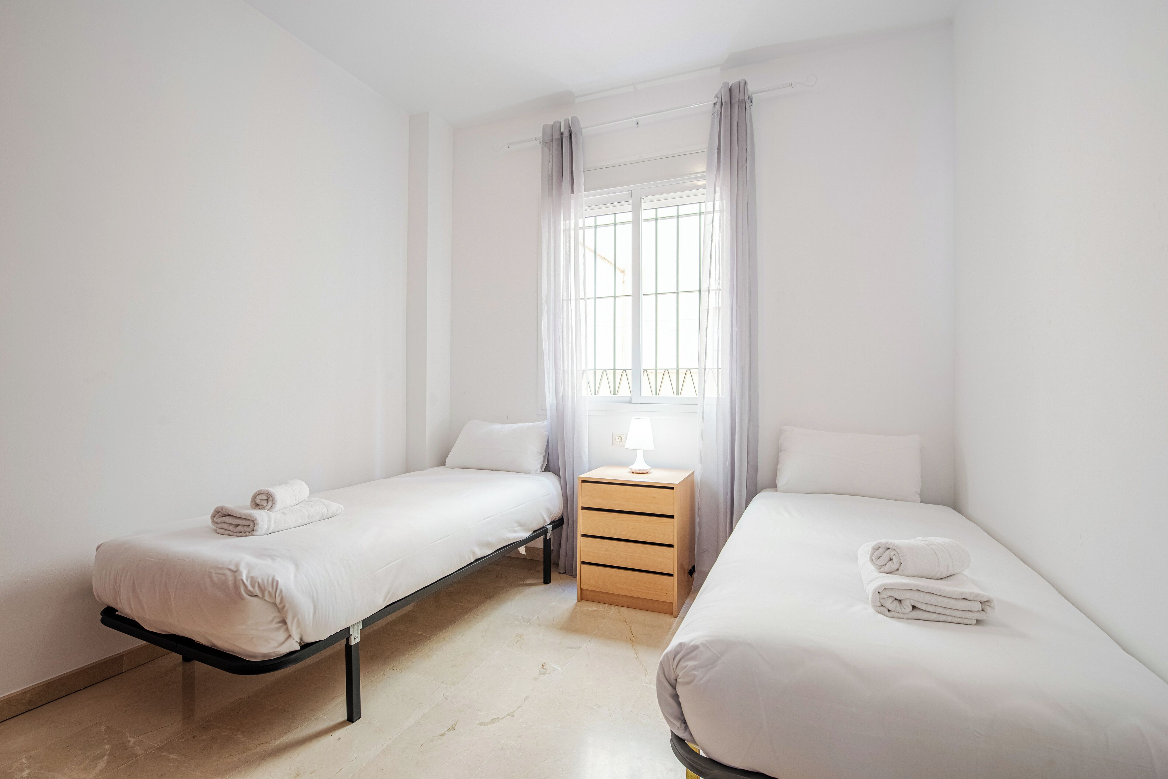 Une chambre avec deux lits simples, une table de chevet en bois avec une lampe et une fenêtre avec des rideaux.