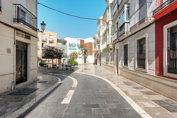 A narrow urban street with buildings on both sides, a bench in the middle, and a clear blue sky. - Stay U-nique Apartment Montaño (Málaga)