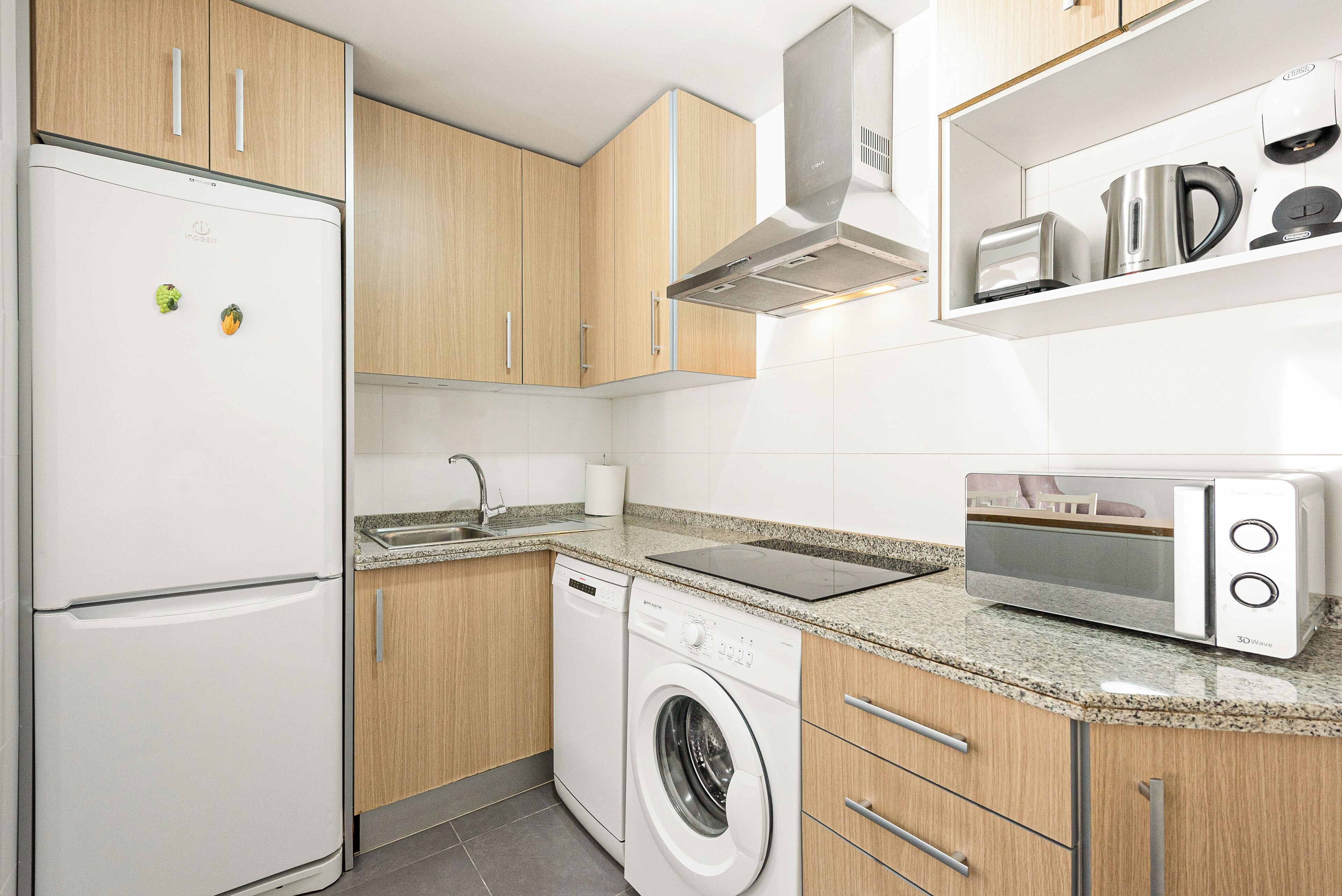 Una cocina compacta con refrigerador, lavadora, microondas y cafetera sobre la encimera.
