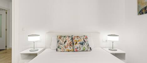 A bedroom with a white bed, two bedside tables with lamps, and a colorful floral pillow.