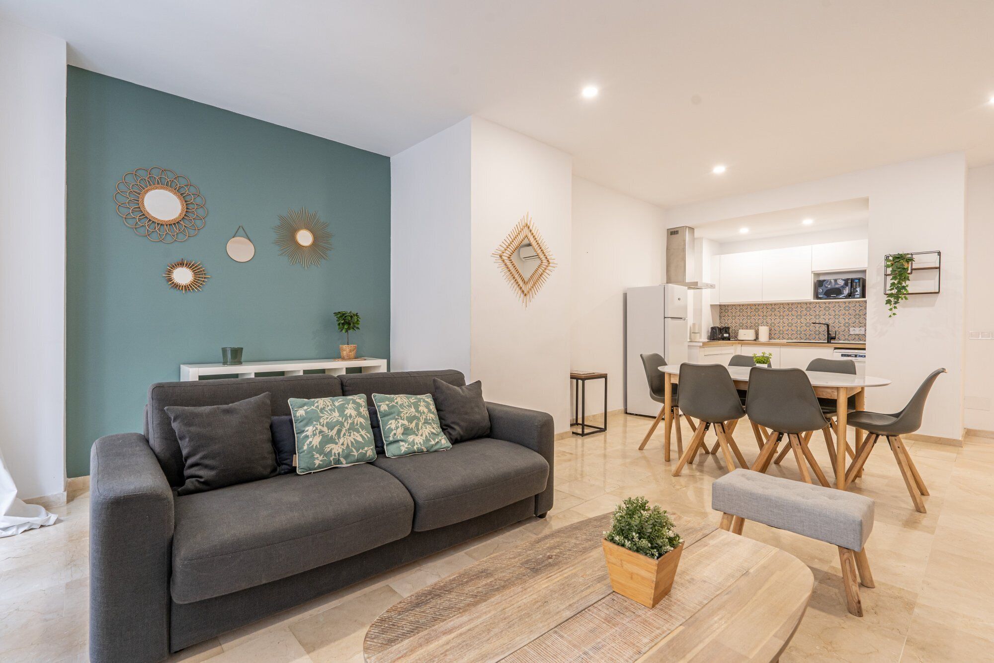 A modern living room with a grey sofa, a coffee table, and a dining area with a white table and chairs.