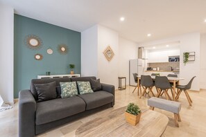 Ein modernes Wohnzimmer mit einem grauen Sofa, einem Couchtisch und einem Essbereich mit weißem Tisch und Stühlen.