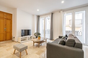 Ein modernes Wohnzimmer mit einem grauen Sofa, einem Holzschrank, einem Fernseher auf einem weißen Schrank und einem Balkon mit Blick.