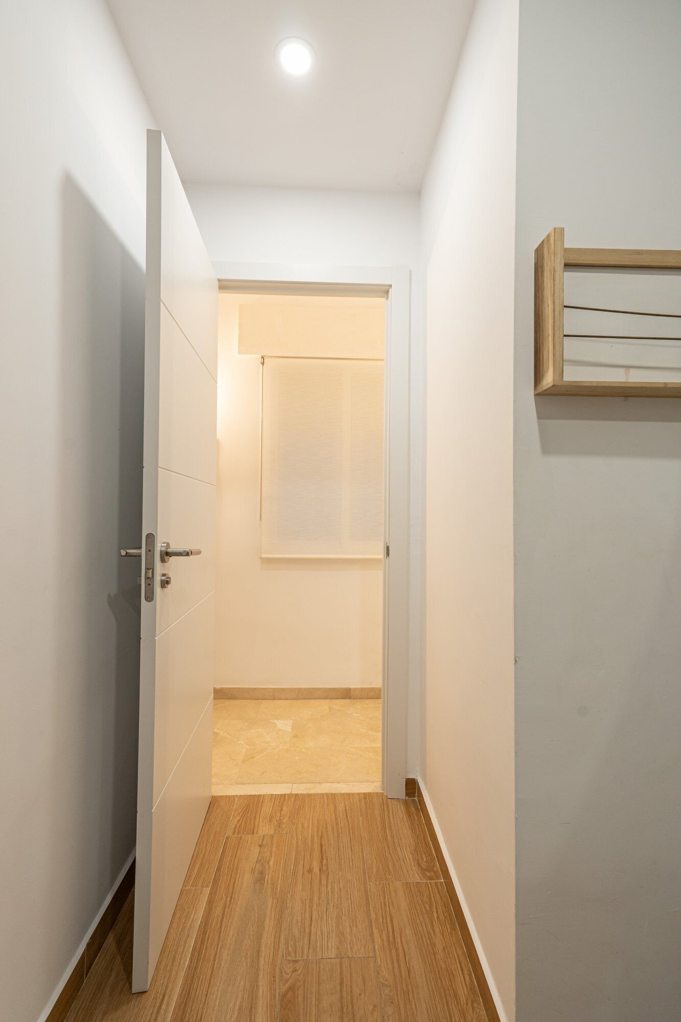 A narrow hallway with wooden flooring, white walls, and a ceiling light.