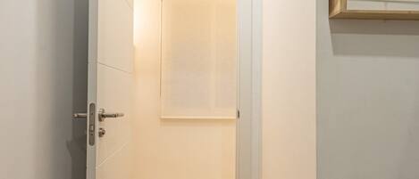 A narrow hallway with wooden flooring, white walls, and a ceiling light.