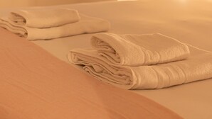 Un lit bien fait, avec des serviettes pliées, et un mur sobre en arrière-plan.
