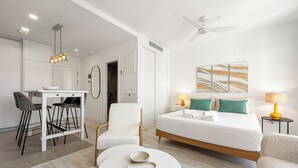 Una habitación de hotel con una cama, un escritorio con una silla, una mesa redonda y un ventilador de techo.