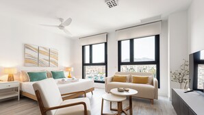 Una habitación de hotel moderna con una cama, dos sofás, una silla, una mesita y un televisor.