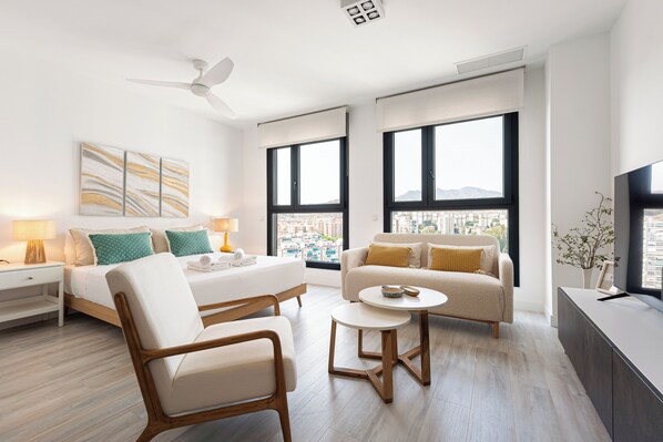 A modern hotel room with a bed, two sofas, a chair, a small table, and a TV. - Stay U-nique Apartments Martiricos (Málaga)