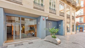 A hotel entrance with a glass door, a small planter with plants, and a tiled pavement. - Stay U-nique Apartment Sebastián Souvirón (Málaga)