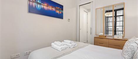 A hotel room with a bed, a nightstand, a mirror, and a painting of a cityscape.
