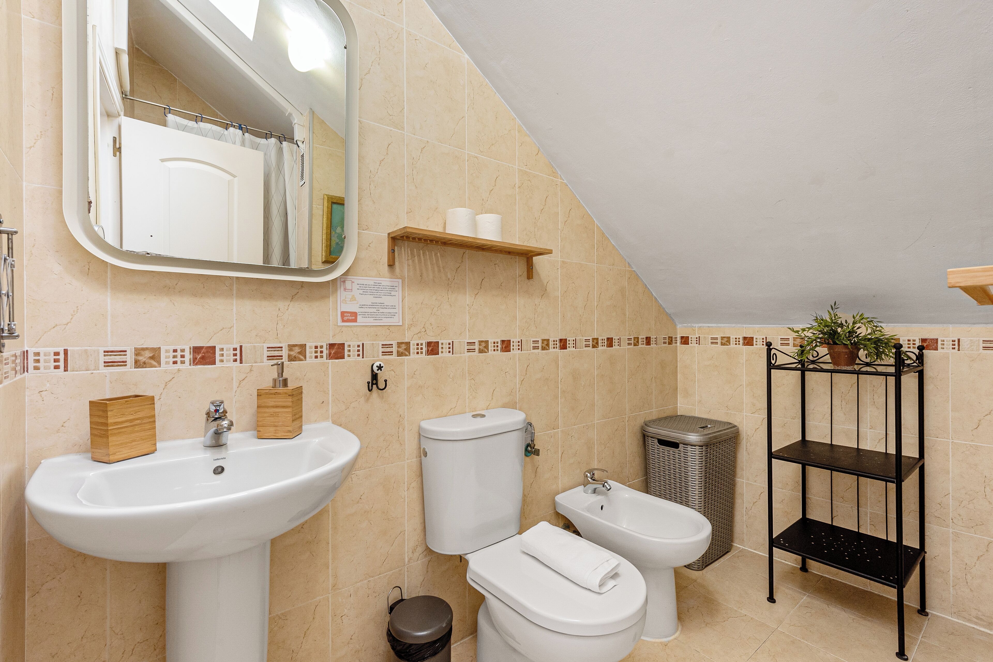 A bathroom with a sink, toilet, bidet, and a shelf with toiletries.