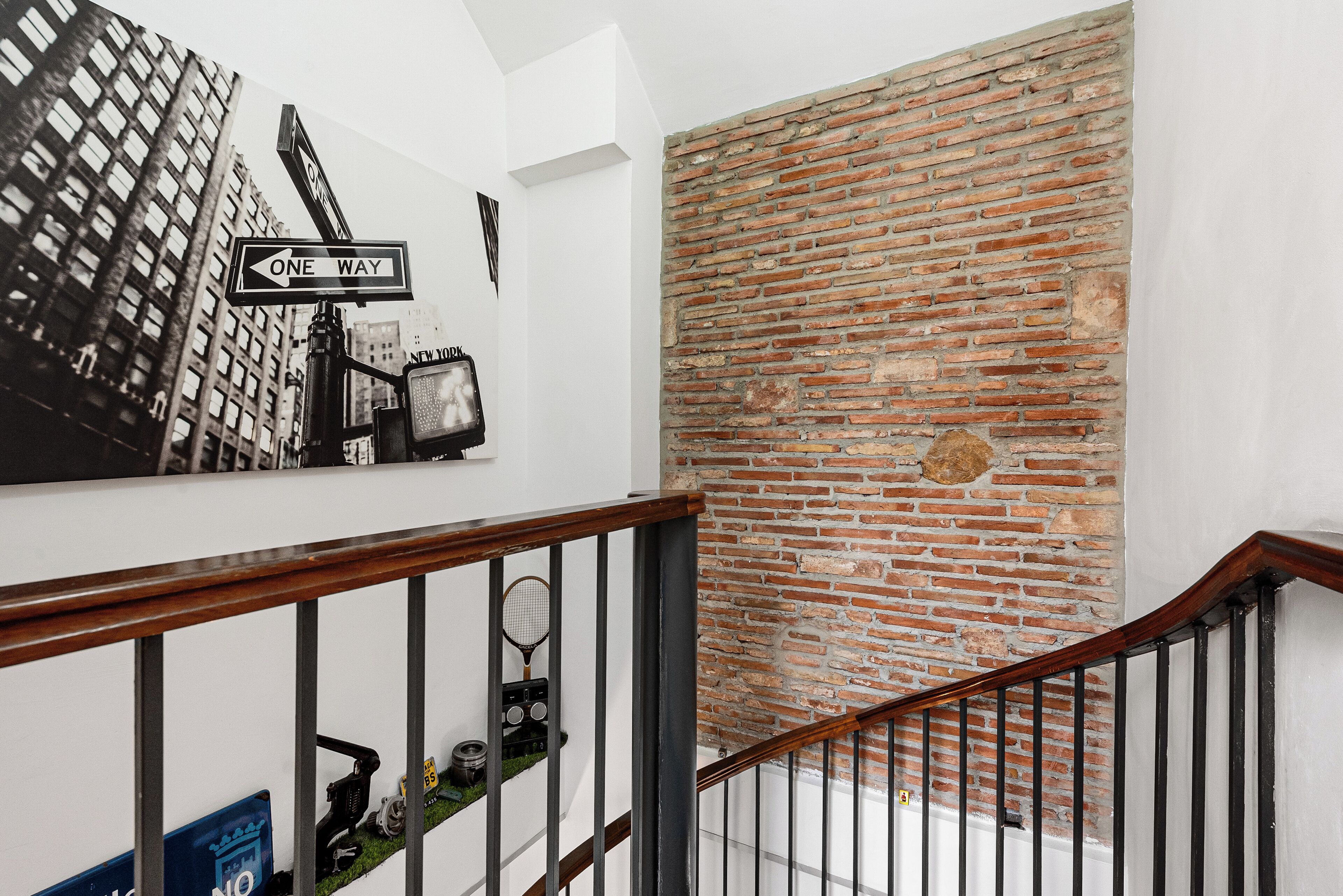 Una scala con corrimano in legno, un muro di mattoni e un cartello con la scritta 'One Way'.