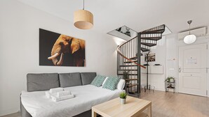 Egy modern nappali, szürke színű kanapéval, fa kávéasztallal, spirál alakú lépcsővel és egy nagyméretű, elefántot ábrázoló műalkotással a falon.