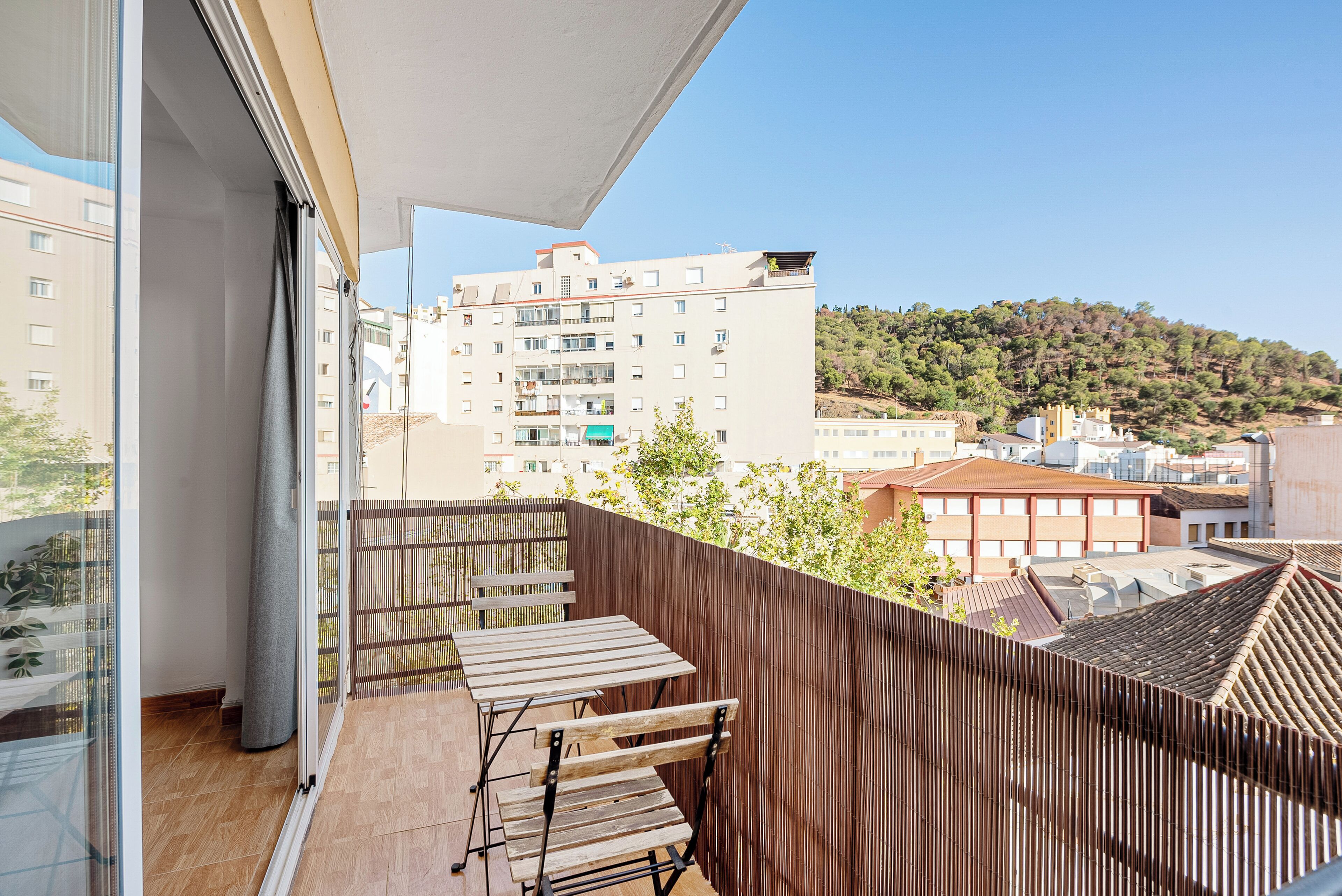 Un balcone con tavolo e sedie in legno, vista su una collina e un edificio sullo sfondo.