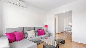 Een moderne woonkamer met een grijze hoekbank, een glazen salontafel en een rode lamp.