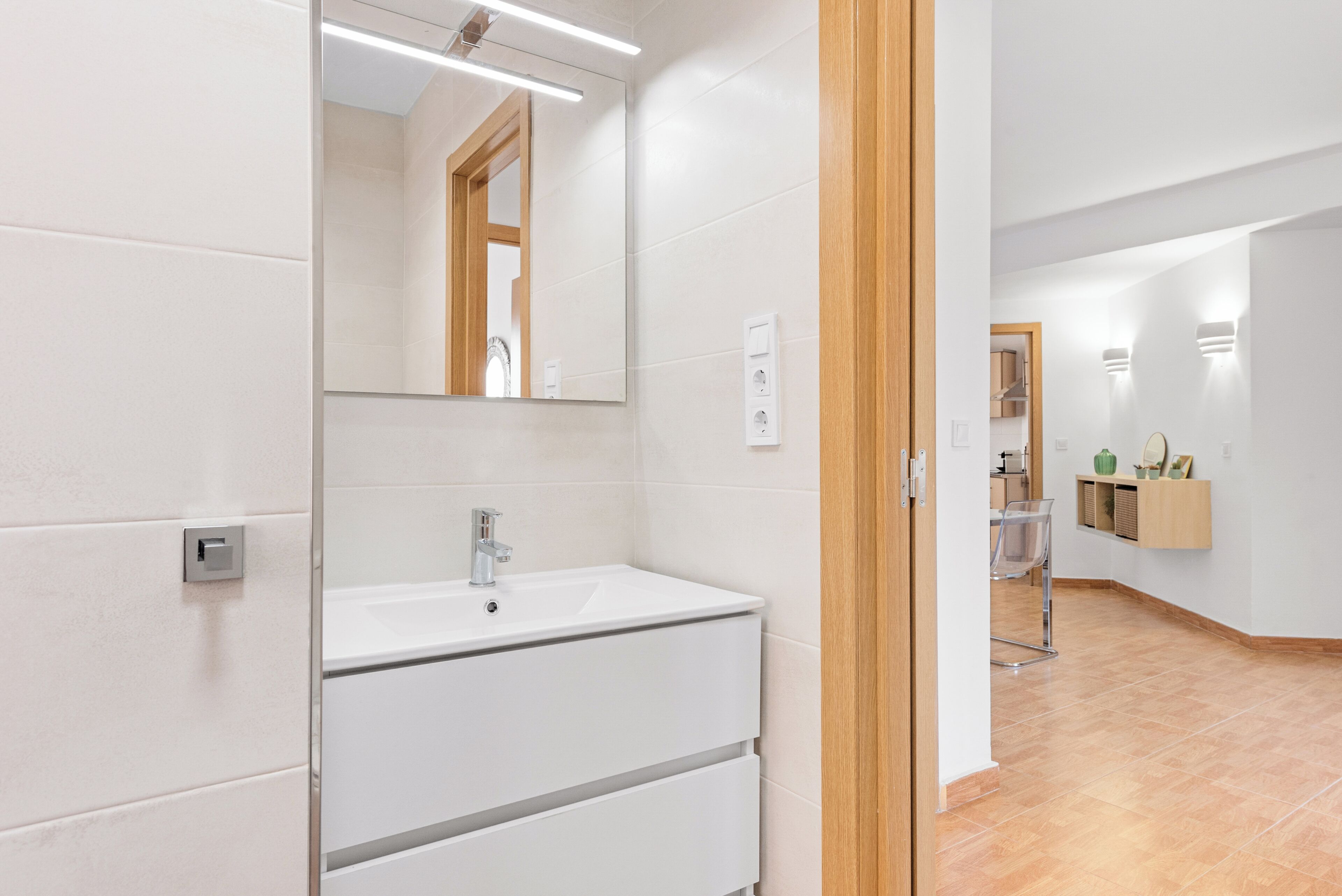 A modern bathroom with a white sink, mirror, and light fixtures.