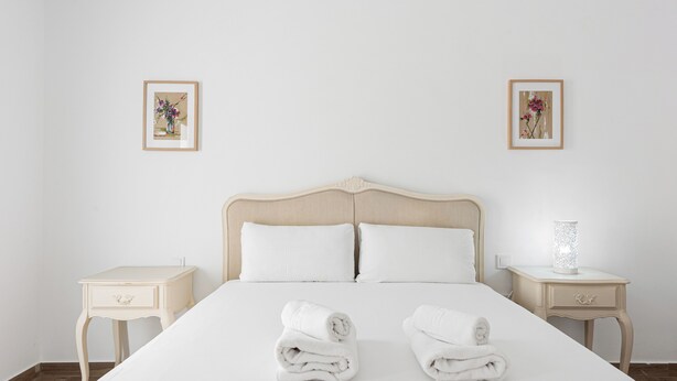 A neatly made bed with two pillows, two bedside tables, and two framed pictures on the wall. - Stay U-nique House Reina Juliana (Málaga)