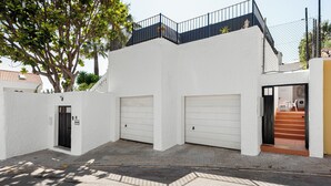 A white building with two garage doors, a staircase leading to a balcony, and a tree in the background. - Stay U-nique House Reina Juliana (Málaga)