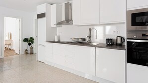 A modern kitchen with white cabinetry, a stainless steel range hood, a built-in oven, and a countertop with a kettle and toaster. - Stay U-nique House Reina Juliana (Málaga)