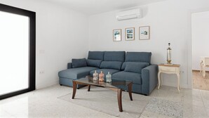A modern living room with a grey sofa, a glass coffee table with decorative items, and a small wooden side table. - Stay U-nique House Reina Juliana (Málaga)