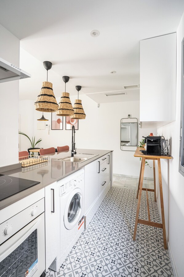 A modern kitchen with a built-in washing machine, a wooden stool, and pendant lights. - Stay U-nique Apartment Plaza del Patrocinio (Málaga)