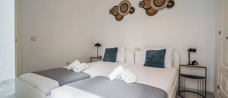 Hotellihuone, jossa on kaksi sänkyä, pieni sivupöytä, seinään kiinnitetty valaisin ja koristeellinen seinätaideteos.