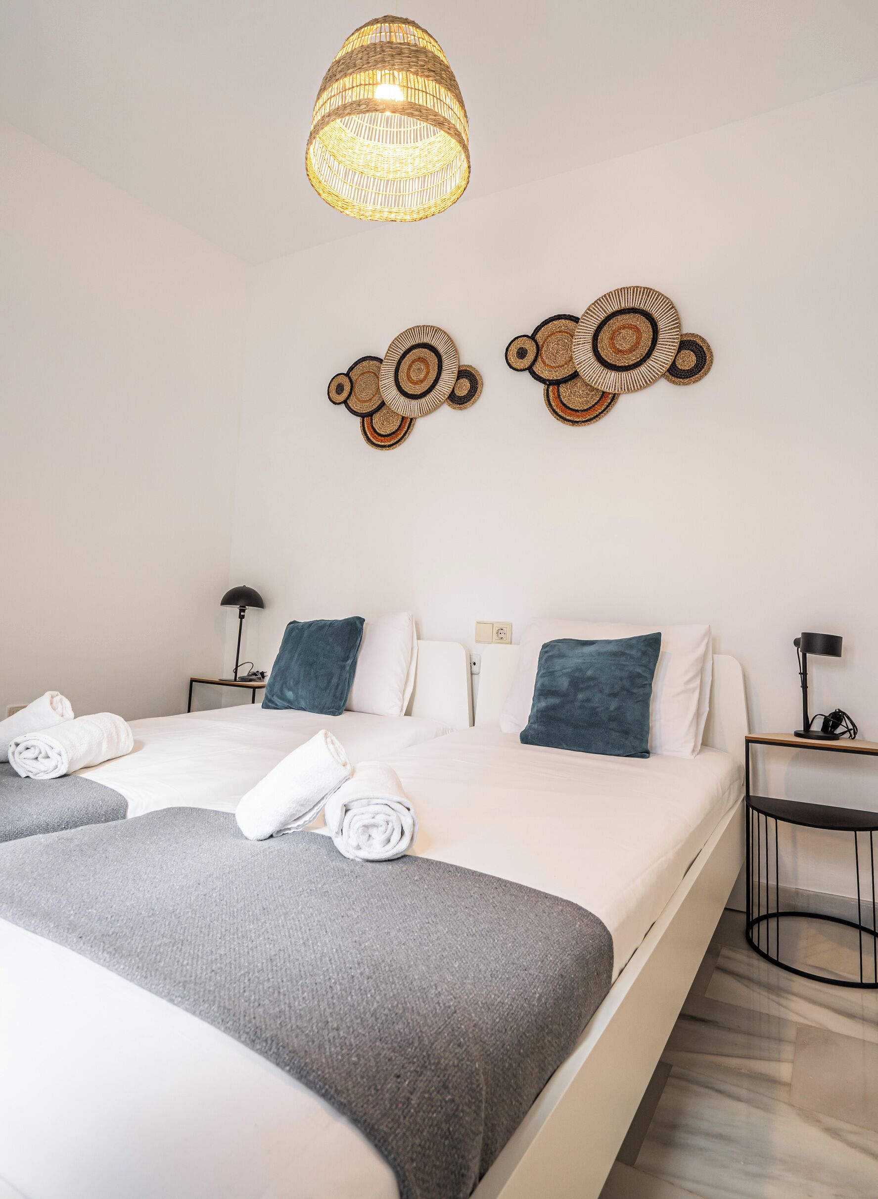 Una habitación de hotel moderna con una cama grande, dos mesitas de noche, una lámpara de fibra y arte decorativo en la pared.