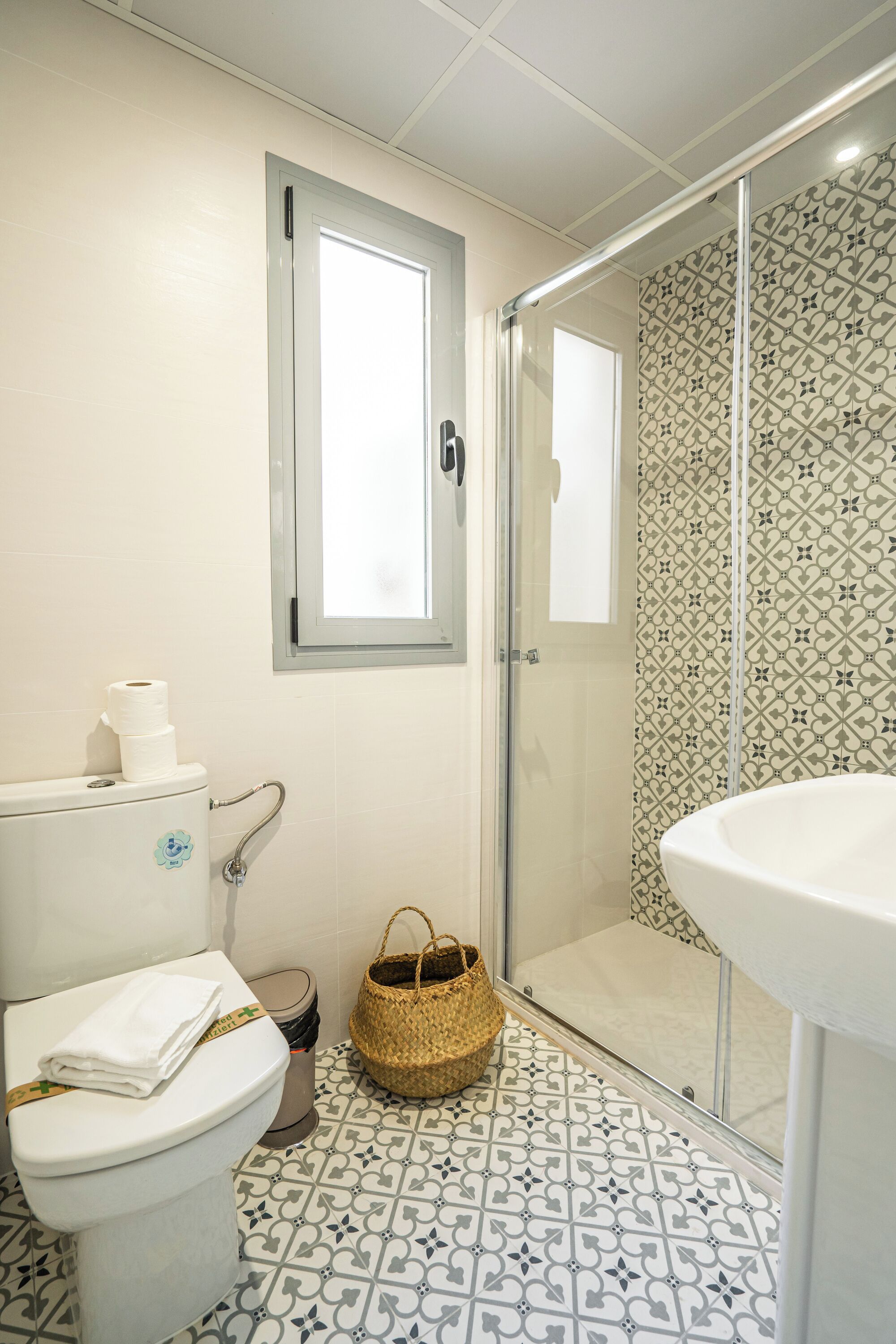 A bathroom with a toilet, a sink, a shower, and patterned floor tiles.