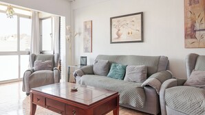 Un salon avec un canapé gris, deux fauteuils, une table basse en bois et un téléviseur posé sur un meuble.