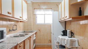 Une cuisine compacte avec des meubles en bois, un évier à deux bacs, un réfrigérateur et une petite table à manger avec des chaises.