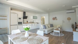 Eine moderne Küche mit weißen Geräten, ein Essbereich mit Tisch und Stühlen sowie ein Wohnzimmer mit Sofa und Dekoration.