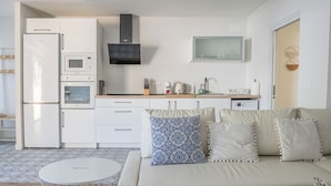 Eine moderne Küche mit weißen Geräten, einem beigen Sofa mit gemusterten Kissen und einem runden gewebten Tisch.