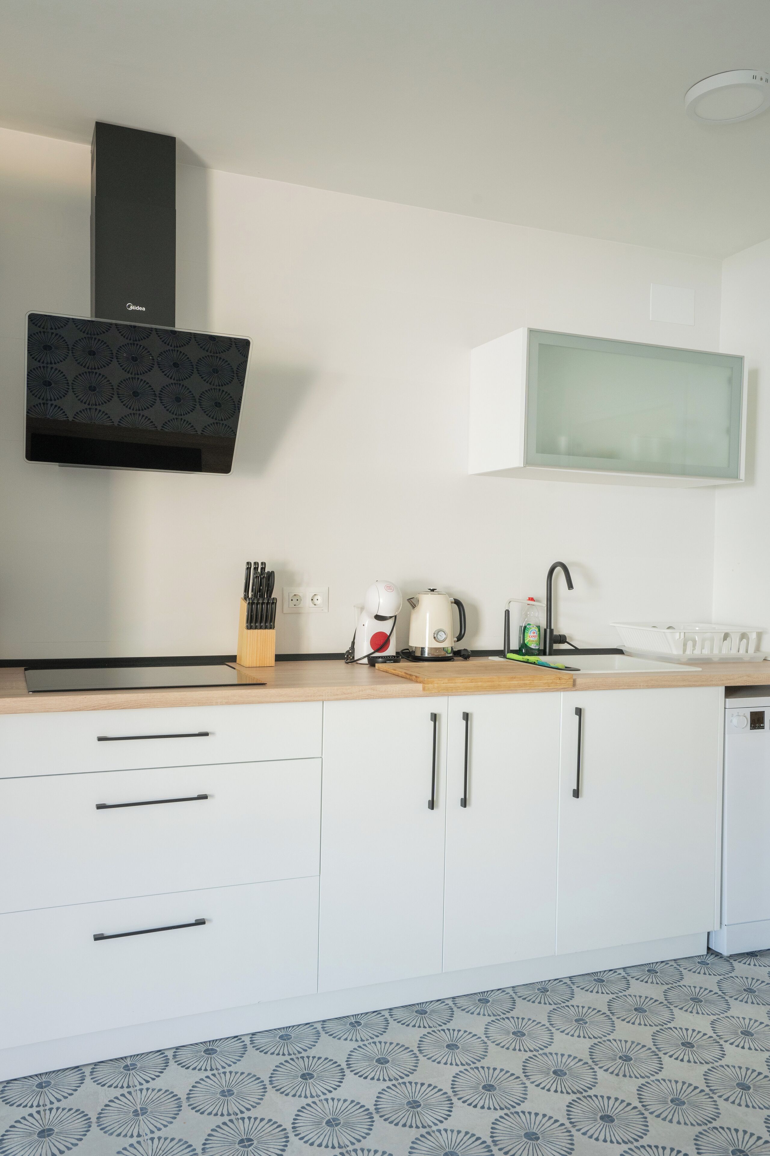 Una cocina moderna con armarios blancos, una campana extractora negra, una cafetera y un hervidor.