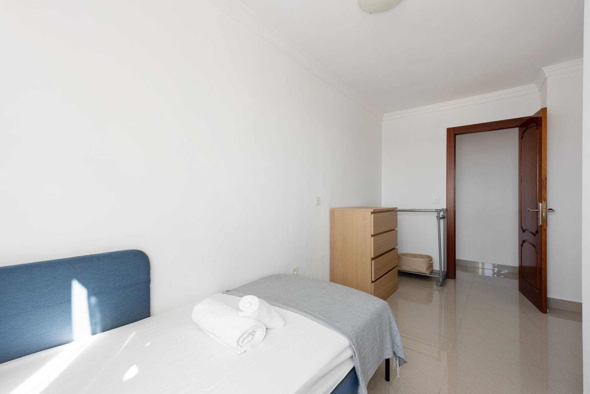 A bedroom with a bed, a dresser, and a door leading to another room.