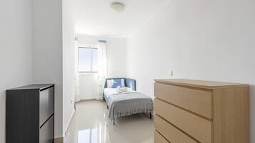 A minimalist bedroom with a bed, a wooden dresser, and a dark cabinet.