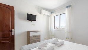 Une chambre d’hôtel avec un lit, une commode en bois, un téléviseur fixé au mur et une fenêtre avec des rideaux.