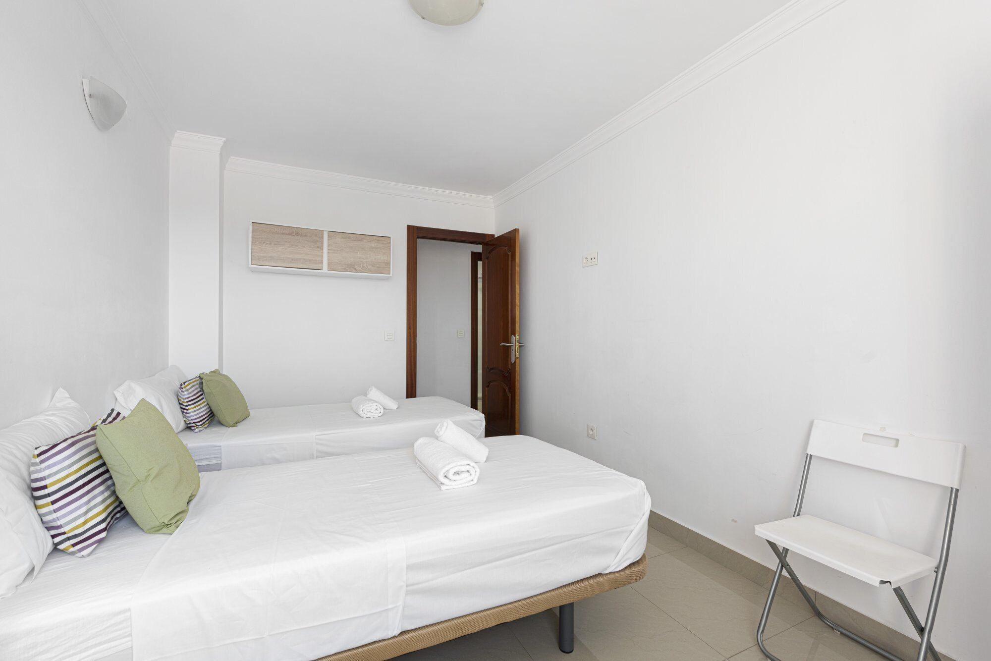 A clean, white room with a bed, a chair, and a door.