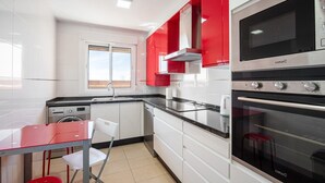 Une cuisine moderne avec des meubles blancs, des touches de rouge, un four en acier inoxydable et une fenêtre.