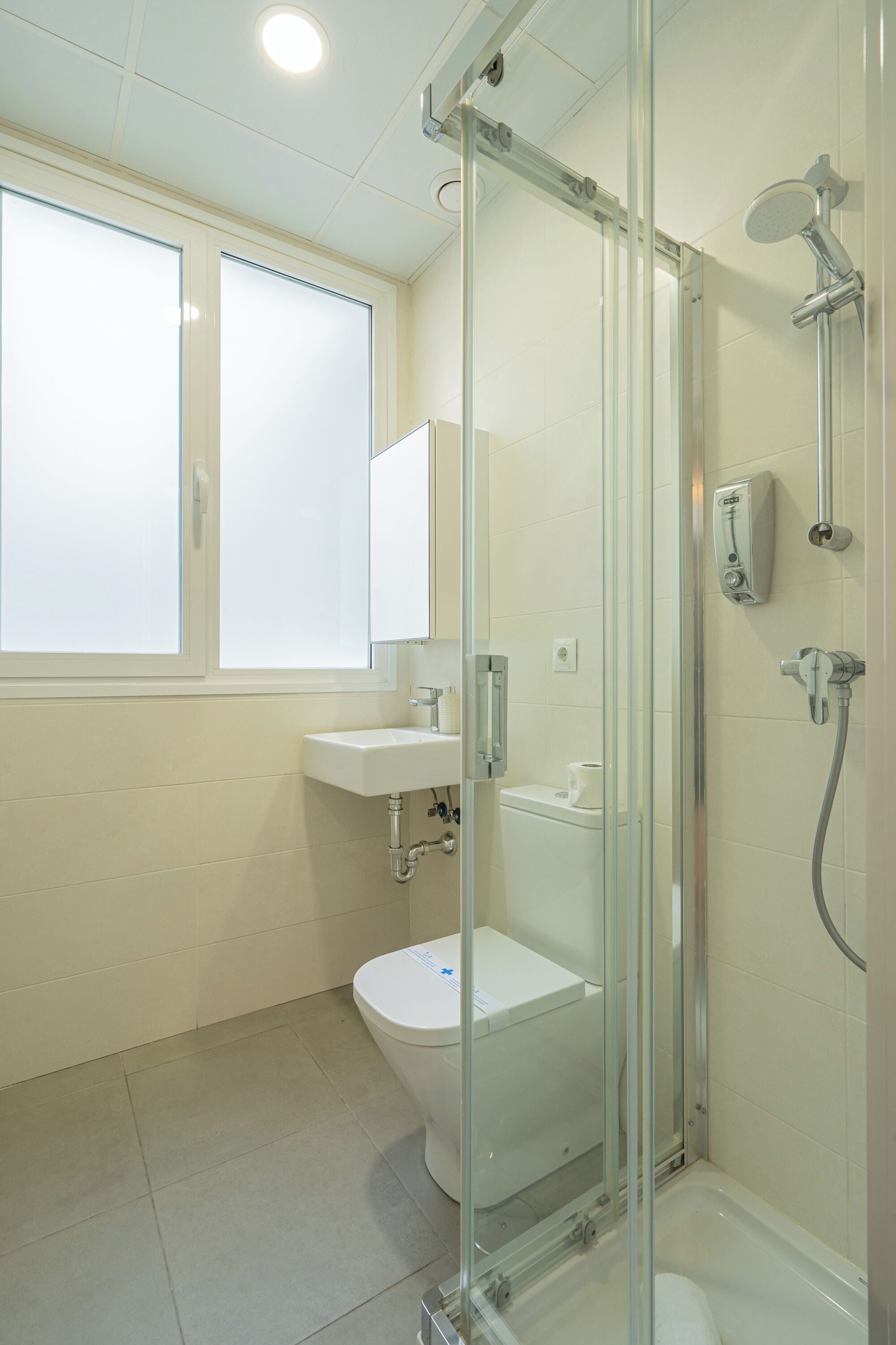 Un baño moderno con ducha de vidrio, lavamanos blanco y retrete.