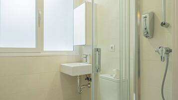 Un baño moderno con ducha de vidrio, lavamanos blanco y retrete.